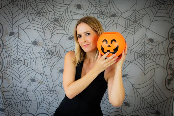 Portrait of beautiful cheerful woman with pumpkin over cobweb background, celebrating halloweens day