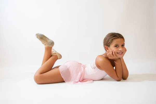 Beautiful little ballerina lying on the floor on white background