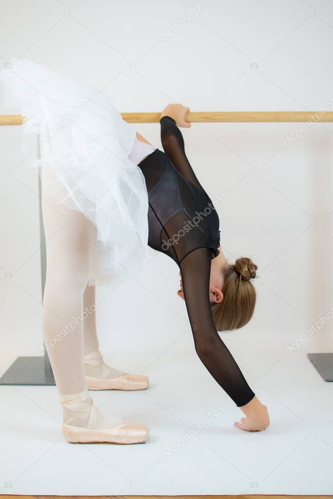 Ballet girl stretching leg in studio. Beautiful tender ballerina having practice in class before performance. School of classical ballet.