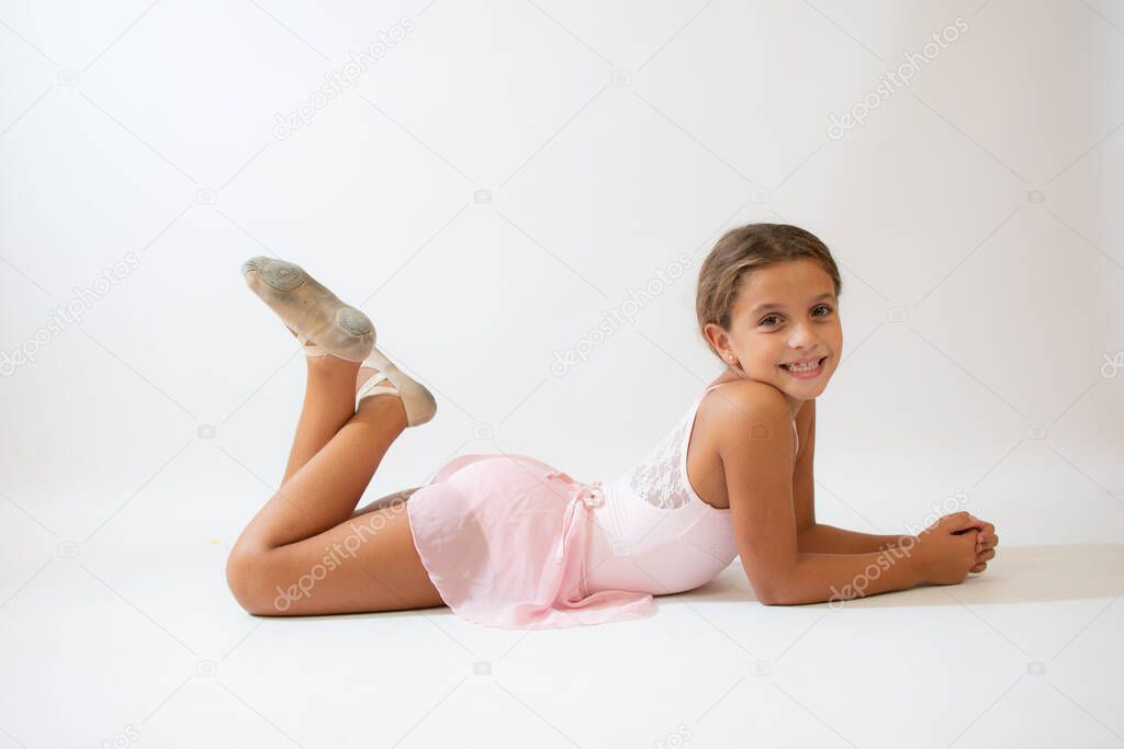 Beautiful little ballerina lying on the floor on white background