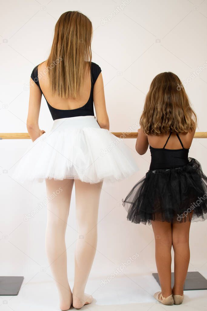 Teacher of the ballet school helps young ballerina perform different choreographic exercises. They rehearse in the ballet class. The teacher communicates with the little girl.