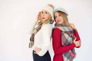 Beyaz duvarın üzerinde poz veren iki kadın. Kış mevsimi. Arkadaşlar birlikte harika zaman geçiriyorlar..