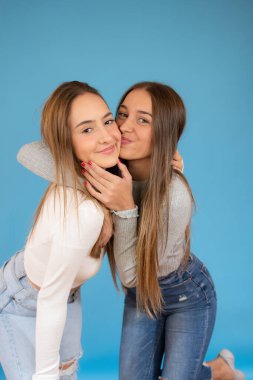 Mutlu gülümseyen genç kızlar mavi arka planda sarılıyorlar.
