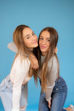 Mutlu gülümseyen genç kızlar mavi arka planda sarılıyorlar.
