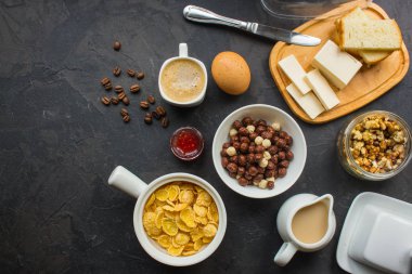 Mısır gevreği, kahve, süzme peynir, ekmek, tereyağı, yumurta, reçel ve diğer malzemeler için karanlık bir arka plan üzerinde kahvaltı. Kopya alanı ile üstten görünüm