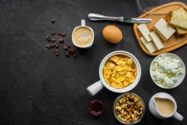 Mısır gevreği, kahve, süzme peynir, ekmek, tereyağı, yumurta, reçel ve diğer malzemeler için karanlık bir arka plan üzerinde kahvaltı. Kopya alanı ile üstten görünüm