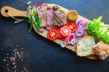 Etli sandviç ve sebzeli burger somun ekmek, domates, marul, orta ya da az pişmiş biftek masanın üzerinde. Üst boy fotokopi alanı, metin yiyecekleri arka planı için.