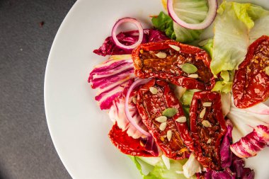 Salata, kurutulmuş domates, yeşil yaprak, soğan, doğal ürün, lezzetli aperatif. Lezzetli gurme yemek arkaplanı, masa, rustik üst manzara, fotokopi alanı, vejetaryen diyeti ve vejetaryen yemeği.