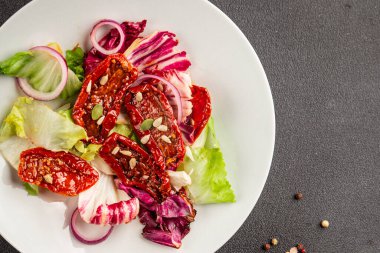 Salata, kurutulmuş domates, yeşil yaprak, soğan, doğal ürün, lezzetli aperatif. Lezzetli gurme yemek arkaplanı, masa, rustik üst manzara, fotokopi alanı, vejetaryen diyeti ve vejetaryen yemeği.