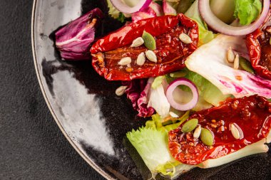 Salata, kurutulmuş domates, yeşil yaprak, soğan, doğal ürün, lezzetli aperatif. Lezzetli gurme yemek arkaplanı, masa, rustik üst manzara, fotokopi alanı, vejetaryen diyeti ve vejetaryen yemeği.