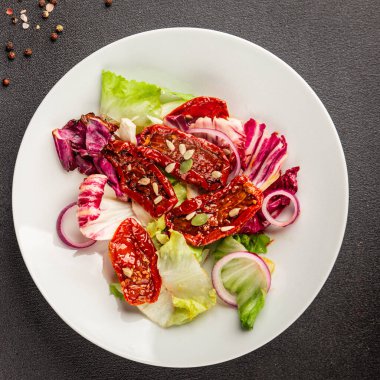 Salata, kurutulmuş domates, yeşil yaprak, soğan, doğal ürün, lezzetli aperatif. Lezzetli gurme yemek arkaplanı, masa, rustik üst manzara, fotokopi alanı, vejetaryen diyeti ve vejetaryen yemeği.