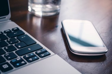 İş Smartphone yanında bir not defteri ve ahşap masa üzerinde bir Glas yansıması ile