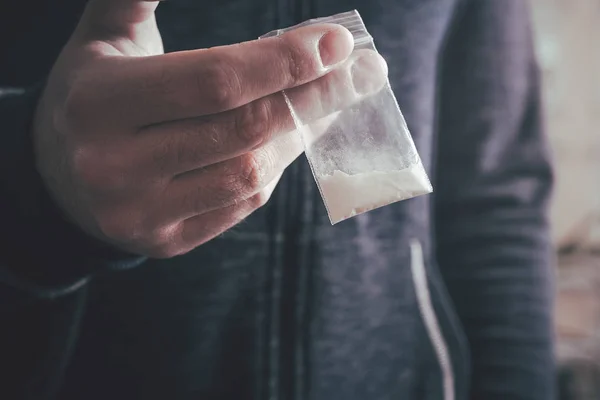 Lidando com drogas por um homem segurando um pequeno saco com pó branco em sua mão — Fotografia de Stock