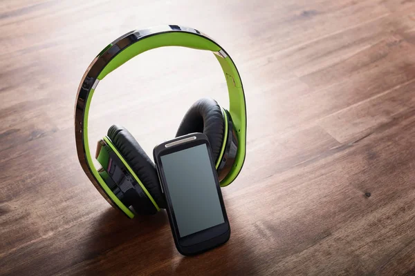 Draadloos luisteren naar muziek Concept met een Smartphone leunend op een grote zwarte Overhead hoofdtelefoon op houten tafel — Stockfoto