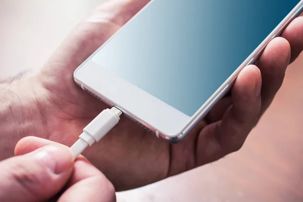 Beyaz bir cep telefonu, Erkek eller tarafından Holded ile beyaz Usb kablosunun bağlı Telifsiz Stok Imajlar