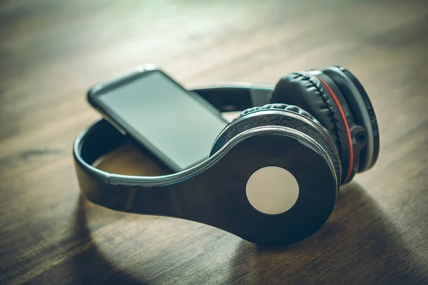 Концепція бездротової слухати музику з чорним мобільним телефоном, що спирається на чорні навушники на дерев'яному столі — стокове фото