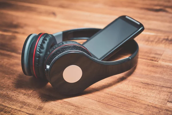 Draadloos luisteren muziek Concept met een zwarte Smartphone leunend op tegen zwarte Overhead hoofdtelefoon op een houten tafel — Stockfoto