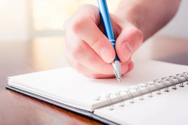 The Front View Of A Male Hand Writing With A Pen In A Blank Book In Front Of A Bright Background