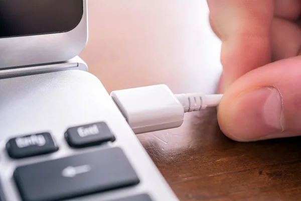 Manlig Hand att dra ut en vit USB-kabel till USB-porten på en bärbar dator Stockbild