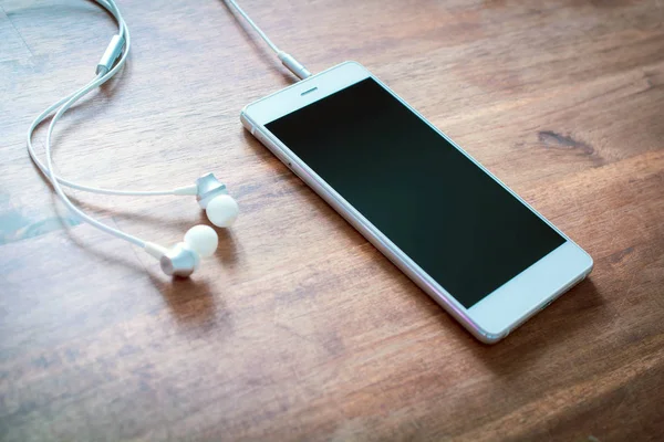 Een witte Smartphone met aangesloten Headset op houten tafel — Stockfoto