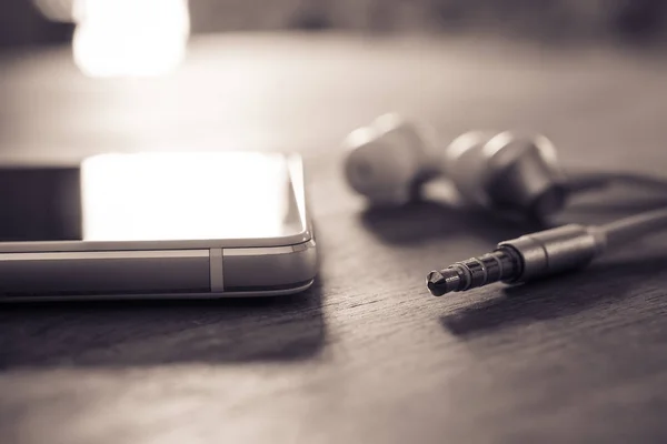 In-Ear hoofdtelefoon en een kabel liggen naast een witte mobiele telefoon In Monochrome kleuren — Stockfoto