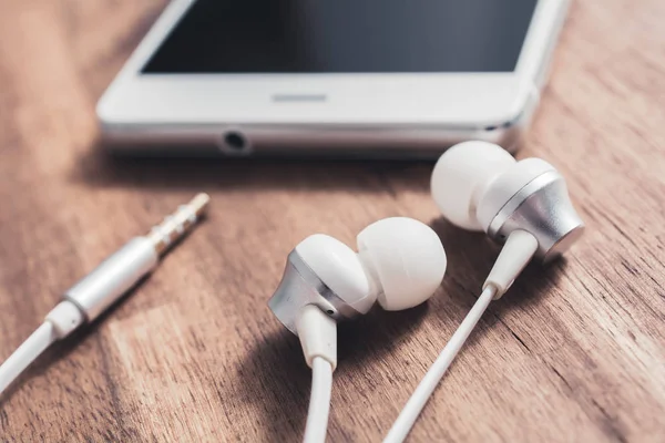 Een In-Ear hoofdtelefoon en de kabel liggen tegenover A wit Smartphones hoofdtelefoonaansluiting — Stockfoto