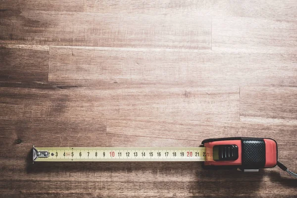 Una cinta métrica sólida con escala extraída acostada en la parte inferior de una mesa de madera, vista de arriba hacia abajo — Foto de Stock