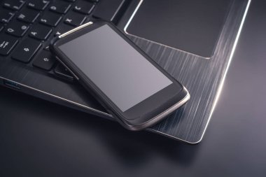 Siyah bir dizüstü bilgisayar, üstten görünüm klavye kenarında yalan yansıması ile siyah Smartphone