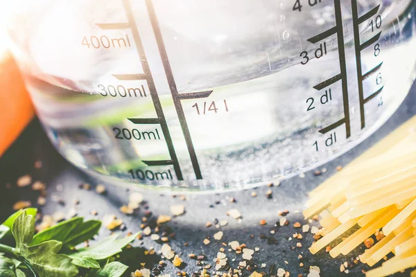 250 ml - ccm Water In A meten Cup omringd door noedels, kruiden en specerijen — Stockfoto