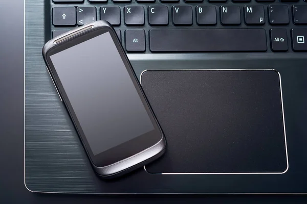 Black Mobile Phone With Reflection Lying On The Left Edge Of The Keyboard Of A Black Notebook, Top View