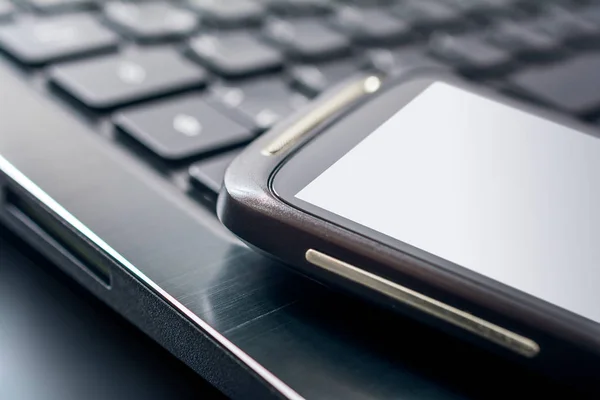 Macro de um telefone celular preto com reflexo deitado na borda esquerda do teclado de um caderno preto, vista superior — Fotografia de Stock