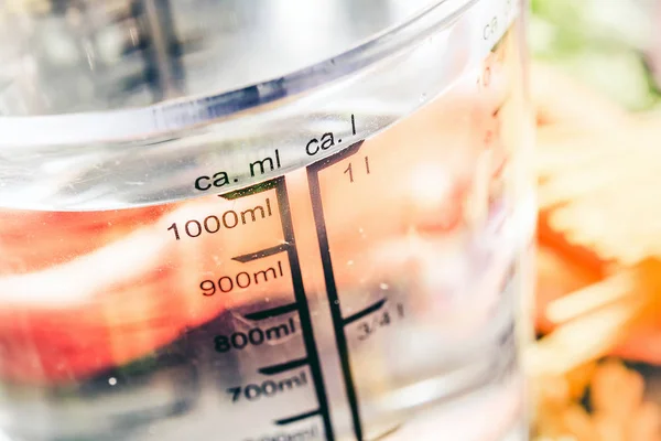 1000 ml - ccm vatten i en mätning Cup omgiven av nudlar, lök, morötter och kryddor Stockfoto