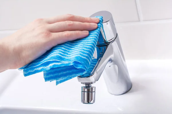 Eine weibliche Hand reinigt den Griff eines Chromhahns mit einem Handtuch im Badezimmer — Stockfoto