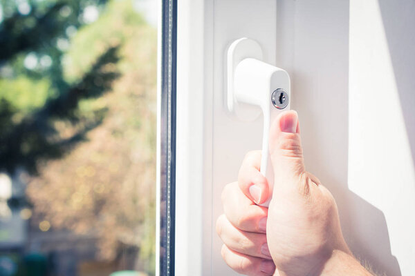 Male Hand Holding A Lockable Window Handle Of A Closed White Window With Trees In Background, Prevent Burglary Concept