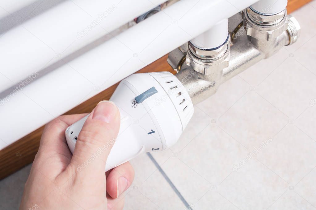 Male Hand Turns The Radiator Of A White Bathroom Heater, Saving Energy Concept
