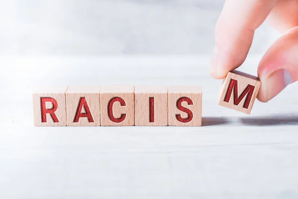 Het woord racisme gevormd door houten blokken en gearrangeerd door mannelijke vingers op een witte tafel — Stockfoto