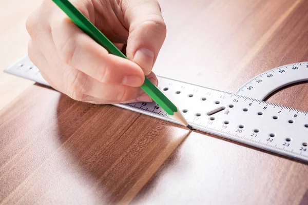 Snickare med hjälp av en gradskiva och göra ett märke vid mätpunkten med en penna på en träskiva — Stockfoto