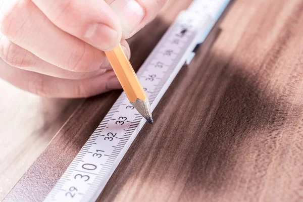 Mano masculina que hace una marca en el punto de medición de un palo de medir plegable en un tablero de madera — Foto de Stock