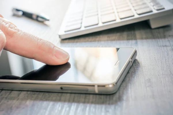 Fingerberührendes Mobiltelefon mit Spiegelung neben weißer Tastatur und Biro auf dem Tisch - Besprechungskonzept für Büros — Stockfoto