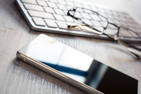 Yansıma, bir çift gözlük ve bir tablo - Office işyeri kavramı üzerinde beyaz bir klavye ile cep telefonu — Stok fotoğraf