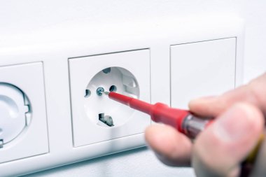 El duvardaki bir prize onarmak için bir aşama Tester tornavida kullanarak bir elektrikçi