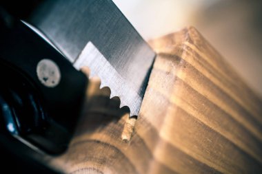 Pürüzlü bir biftek bıçağı makro kısmen bir mutfak Knive bloğundan bir masanın üzerine çekti.