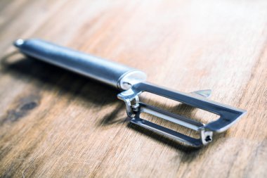 Ahşap bir masaya uzanmış bir paslanmaz sebze soyucu