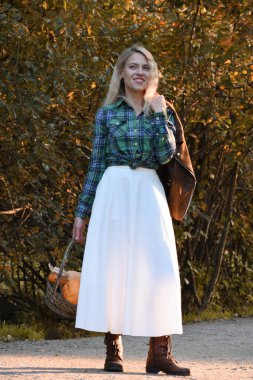 Kırsal tarzda giyinmiş bir kız elinde bir sepet balkabağıyla sonbahar ormanı yolunda duruyor..