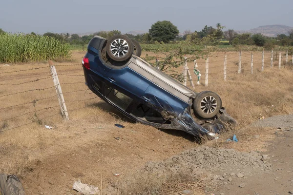 Photo of a car that is crashed and flipped before falling on a roadside in a rural area