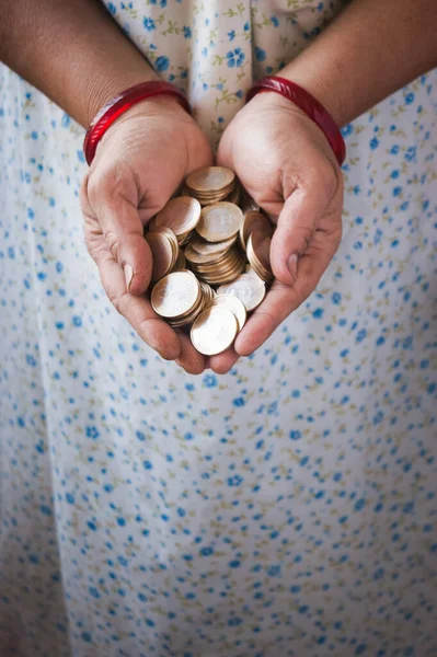 A vertical image of a middle aged lady holding lots of coins in her hands