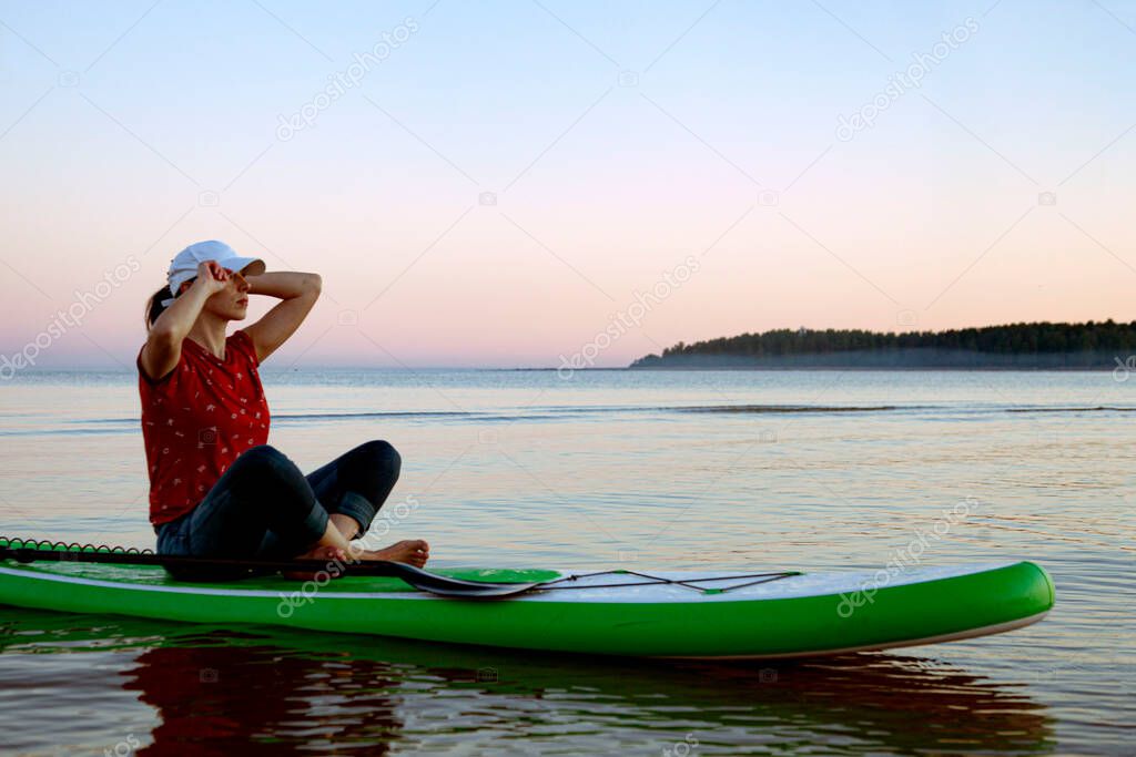Girl in the sea at sunset sitting calmly on a surfboard. Sup board. 