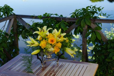 Gölün kenarındaki bir masada sarı çiçek aranjmanı, çiçekler.