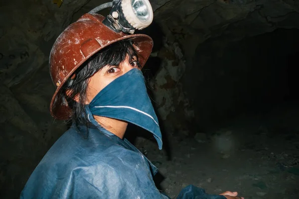 Woman miner with scarf on her face and protective helmet with light in a mine tunnel
