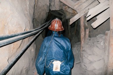 Miner with helmet and light by tunnel in silver mine, seen from behind clipart